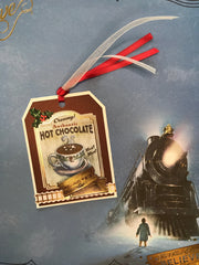 craft kit featuring a hot chocolate gift tag shown with red ribbon on top of a scrapbook paper of the Polar Express from the paper crafting kit.